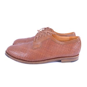May include: A pair of brown leather shoes with a woven pattern. The shoes have lace-up closures and a slightly rounded toe.
