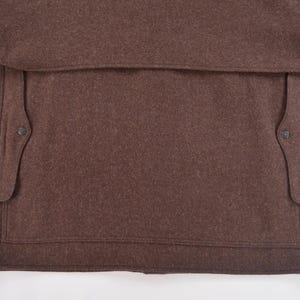 May include: Close-up of a brown wool coat. The coat features a large pocket and two smaller pockets with button closures. A classic design, suitable for cold weather, made from wool.