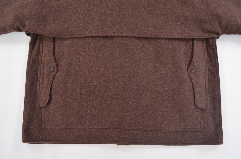 May include: Close-up of a brown wool coat. The coat features a large pocket and two smaller pockets with button closures. A classic design, suitable for cold weather, made from wool.