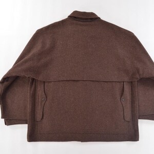 May include: A brown wool jacket with a collar and two front pockets. The jacket features a cape-like design over the shoulders and a button closure. The garment is displayed on a white background.