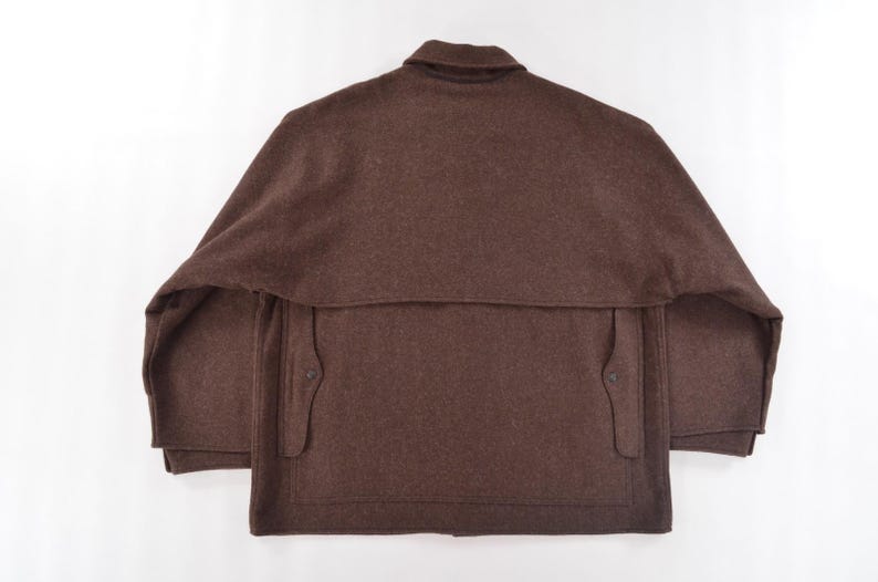 May include: A brown wool jacket with a collar and two front pockets. The jacket features a cape-like design over the shoulders and a button closure. The garment is displayed on a white background.