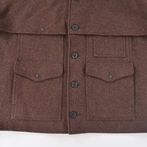 May include: A brown wool jacket with a button-up front and four front pockets. The jacket has a collar and a flap over the shoulders. The jacket is made of a thick, warm material.