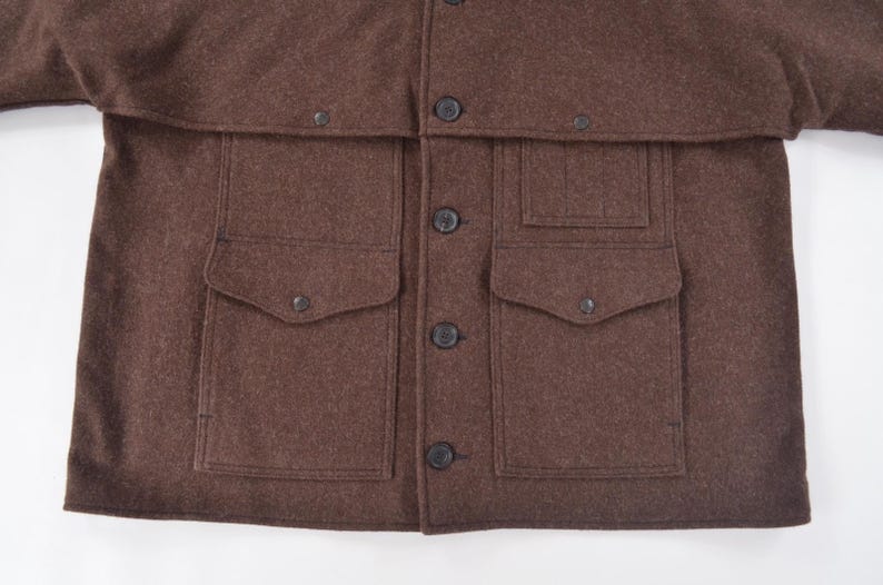 May include: A brown wool jacket with a button-up front and four front pockets. The jacket has a collar and a flap over the shoulders. The jacket is made of a thick, warm material.