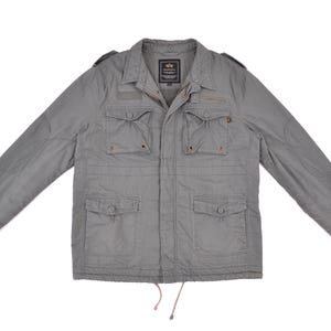 Könnte beinhalten: Eine graue Utility-Jacke mit mehreren Taschen und einem Reißverschluss. Die Jacke hat einen Kordelzug am unteren Rand und ein Markenetikett auf der Brust.