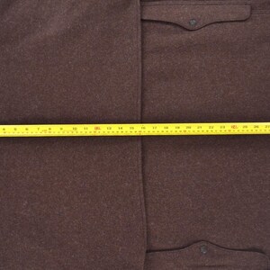 May include: A brown wool coat with two front pockets and a button closure. The coat is measured with a yellow tape measure, showing a length of approximately 81 cm.