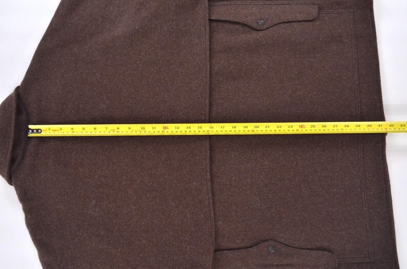 May include: A brown wool coat with two front pockets and a button closure. The coat is measured with a yellow tape measure, showing a length of approximately 81 cm.