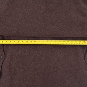 May include: A brown coat with a yellow measuring tape across the front. The coat has two pockets and a button on each pocket. The measuring tape shows a length of approximately 76 cm.