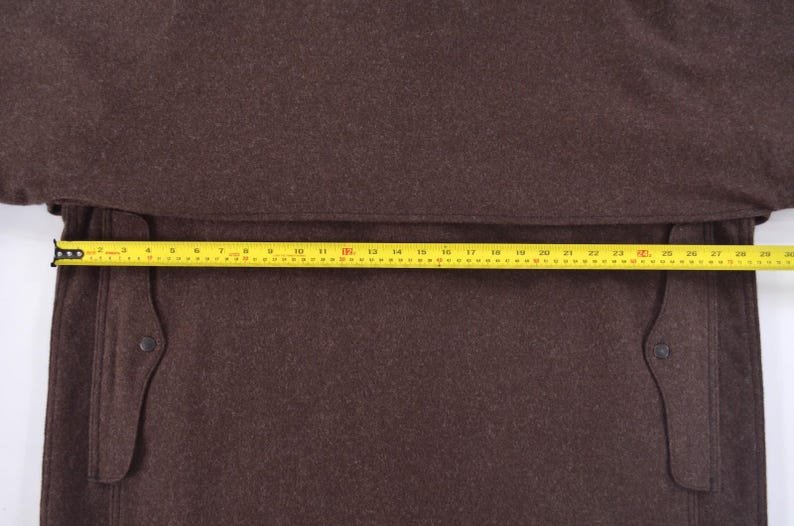 May include: A brown coat with a yellow measuring tape across the front. The coat has two pockets and a button on each pocket. The measuring tape shows a length of approximately 76 cm.