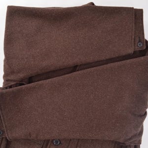 May include: A folded brown wool coat with button details. The coat is a solid colour and appears to be made of a thick, warm material. The sleeves are folded over, and the buttons are visible.