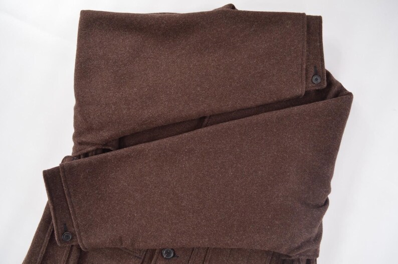 May include: A folded brown wool coat with button details. The coat is a solid colour and appears to be made of a thick, warm material. The sleeves are folded over, and the buttons are visible.