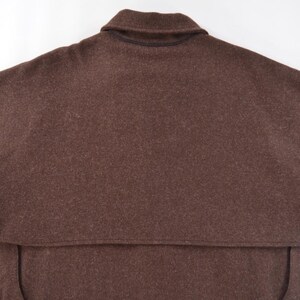 May include: A brown wool cape with a collar. The cape has a wide, flowing design, with a capelet over the shoulders. The fabric appears to be a solid, dark brown colour. The garment is likely outerwear.