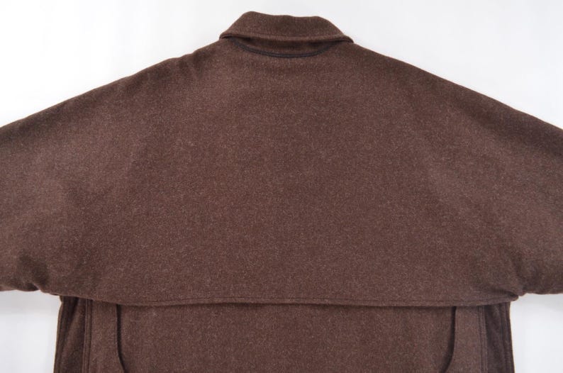 May include: A brown wool cape with a collar. The cape has a wide, flowing design, with a capelet over the shoulders. The fabric appears to be a solid, dark brown colour. The garment is likely outerwear.