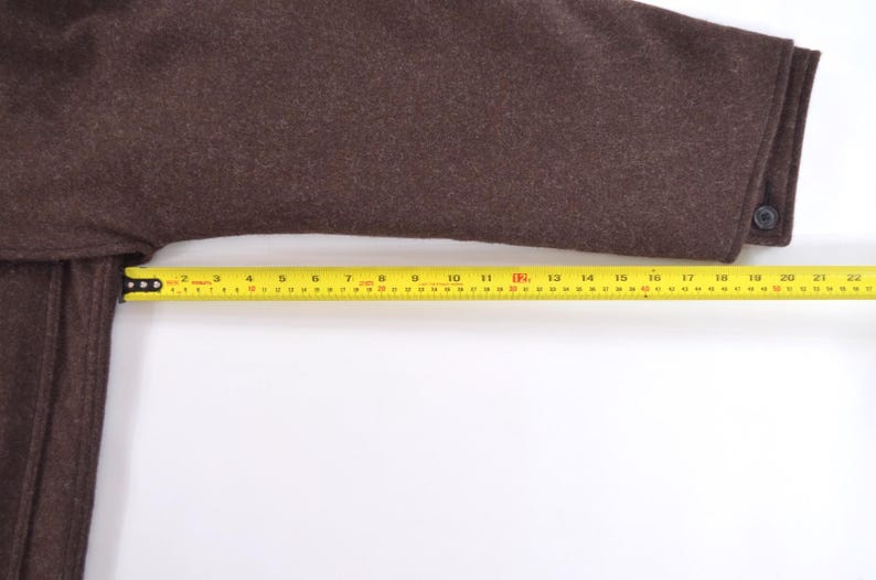 May include: A brown wool coat sleeve with a buttoned cuff. A yellow tape measure shows the sleeve's length. The sleeve measures approximately 56 cm from cuff to shoulder.