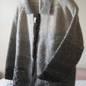 May include: A brown, gray, and white knitted cardigan with a collar and button closure. The cardigan has a gradient pattern and a cable knit design on the bottom.