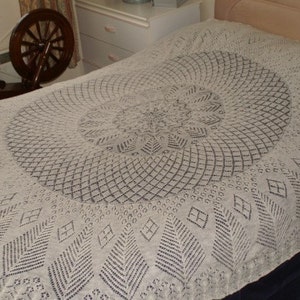 Könnte beinhalten: Eine weiße Häkelbettdecke mit einem runden Design in der Mitte. Das Design zeigt ein sich wiederholendes Muster aus kleinen Quadraten und Rauten.