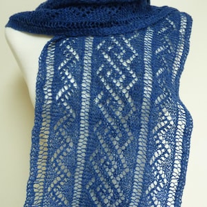 May include: A blue knitted scarf with a lacy pattern. The scarf is displayed on a white mannequin.