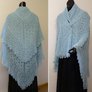 Könnte beinhalten: Ein hellblauer gestrickter Schal mit einem zarten Spitzenmuster. Der Schal ist über eine Schaufensterpuppe gelegt und von vorne und hinten zu sehen.