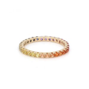 May include: A gold band ring with a rainbow of gemstones set in a continuous line around the band.
