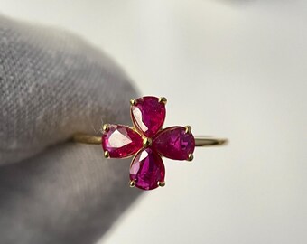 Puede incluir: Un anillo de oro con un diseño de flor de cuatro pétalos. Cada pétalo es un rubí vibrante en forma de pera, que irradia un tono rojo intenso. La banda del anillo es delgada y pulida, creando una joya delicada y elegante.