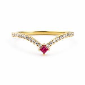 May include: A gold ring featuring a V-shaped design. The ring is embellished with small, clear gemstones along the curved edges and a square, red gemstone at the centre. The ring is set against a white background.