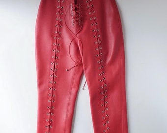 May include: Red leather trousers with lace-up detailing on the sides. The laces are red and the eyelets are silver.