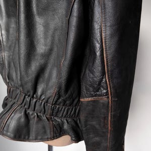 May include: Close-up of a black leather jacket with visible wear and tear. The jacket has a cinched waist and detailed stitching along the seams. The leather appears distressed with brown accents.