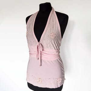 Puede incluir: Un top halter de color rosa claro con un escote en V profundo y cierre de lazo frontal. La prenda está adornada con intrincados bordados florales y abalorios a lo largo del escote y el dobladillo inferior, con un panel de cintura fruncido.