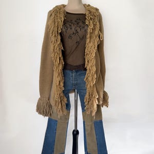 Könnte beinhalten: Drei cremefarbene Keramikbecher mit gesprenkelter Glasur. Jeder Becher zeigt ein handgemaltes Blumenmuster in Blau-, Grün- und Gelbtönen. Die Becher haben eine einfache, abgerundete Form und einen Henkel.