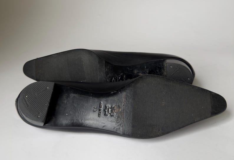May include: Black leather shoes with a pointed toe and a rubber sole. The shoes have a size 39 label on the sole.