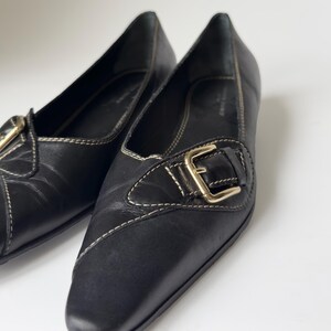 May include: A pair of black leather flats with a gold buckle. The shoes have a pointed toe and a low heel.