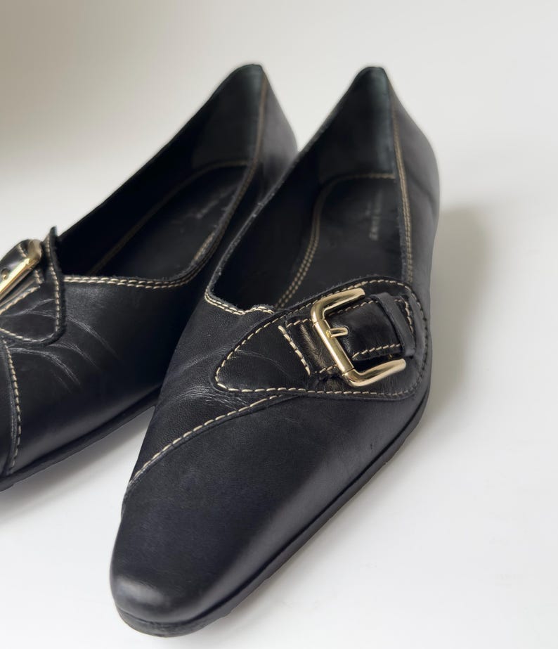 May include: A pair of black leather flats with a gold buckle. The shoes have a pointed toe and a low heel.