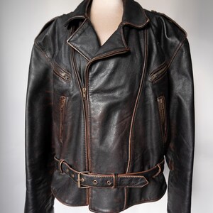 May include: A black leather jacket with a brown distressed finish. The jacket features a notched collar, a front zipper closure, and multiple zippered pockets. It has a belt at the waist and is displayed on a mannequin.