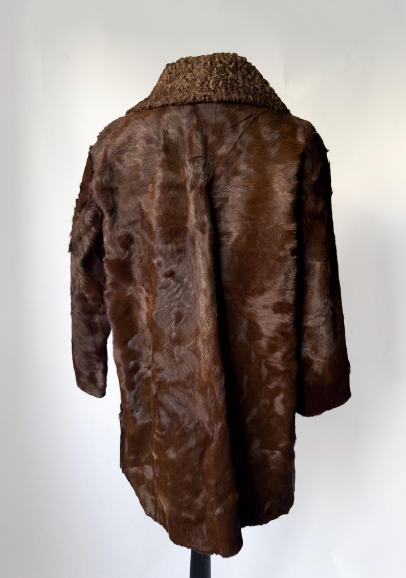 May include: A brown fur coat with a textured collar. The coat is a dark shade of brown and appears to be made of animal fur. The coat is displayed on a black stand against a white background.