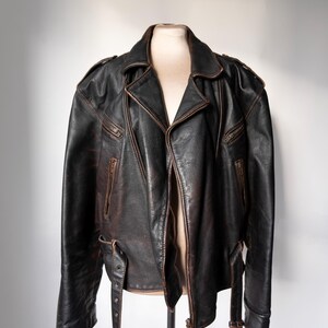 May include: A black leather motorcycle jacket with a classic asymmetrical zip closure. The jacket features multiple zippered pockets, shoulder epaulets, and a notched lapel. The leather has a distressed appearance with brown accents, and adjustable waist belts.