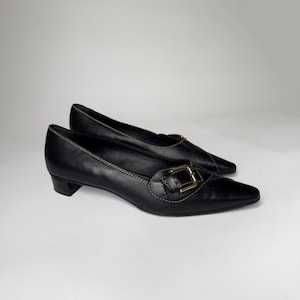 May include: Black leather heeled shoes with a gold buckle and pointed toe.