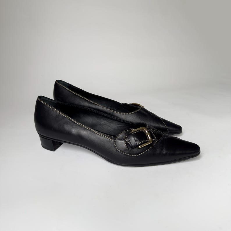 May include: Black leather heeled shoes with a gold buckle and pointed toe.