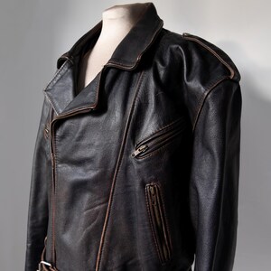 May include: A dark brown leather jacket with a classic asymmetrical zipper design. The jacket features a notched collar, shoulder epaulets, and a zippered chest pocket. The leather has a distressed appearance.