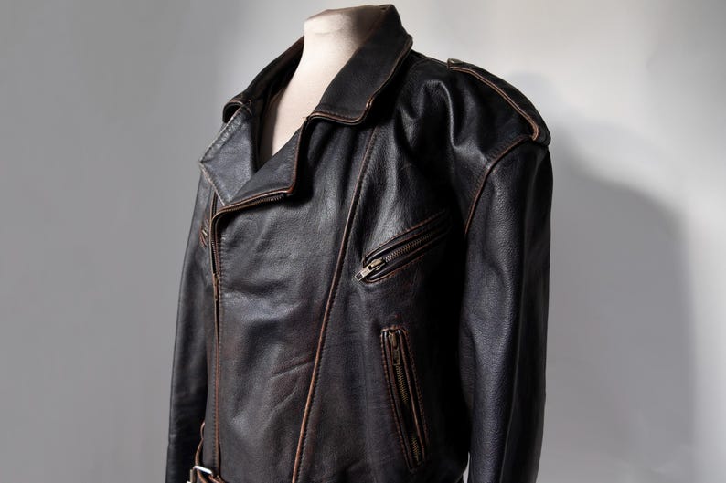 May include: A dark brown leather jacket with a classic asymmetrical zipper design. The jacket features a notched collar, shoulder epaulets, and a zippered chest pocket. The leather has a distressed appearance.