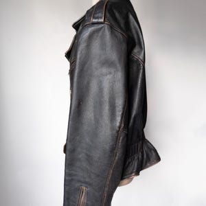 May include: Black leather jacket with a classic design. The jacket features a notched collar, a zipper closure, and a fitted silhouette. The leather has a distressed look with brown accents, giving it a vintage feel.