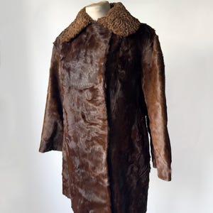 May include: A vintage brown fur coat with a textured collar and long sleeves. The coat is displayed on a mannequin against a white background. The fur appears to be a rich, dark brown color.
