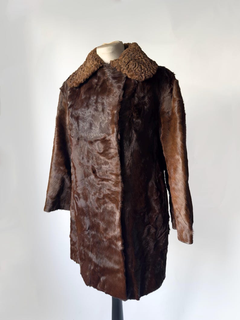 May include: A vintage brown fur coat with a textured collar and long sleeves. The coat is displayed on a mannequin against a white background. The fur appears to be a rich, dark brown color.