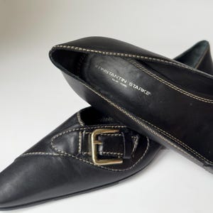 May include: Black leather flats with a gold buckle and a pointed toe. The shoes are by the brand Konstantin Starke, New York.