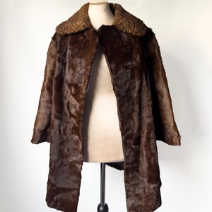 May include: A brown fur coat with a textured collar and a long, open front. The coat is displayed on a mannequin against a white background. The fur appears to be a dark shade of brown.
