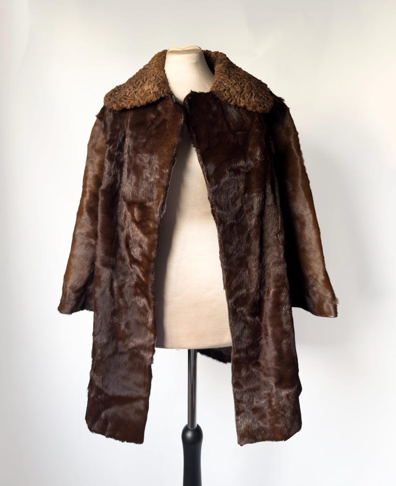 May include: A brown fur coat with a textured collar and a long, open front. The coat is displayed on a mannequin against a white background. The fur appears to be a dark shade of brown.