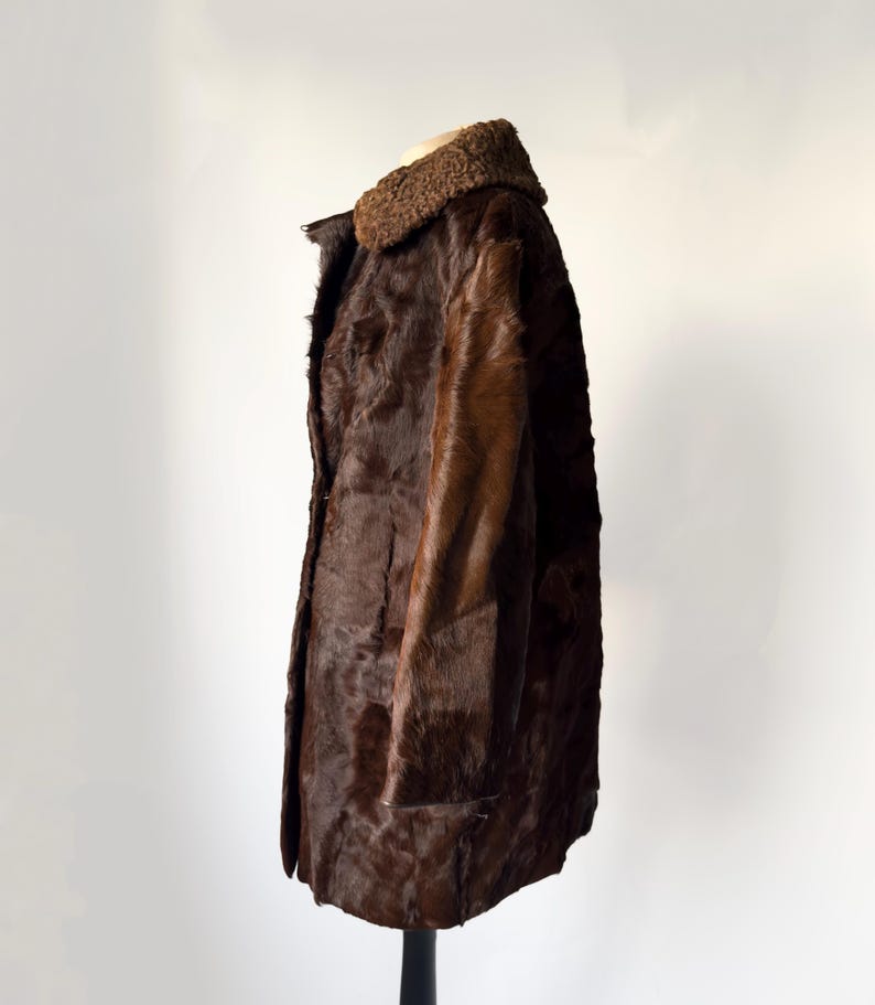 May include: A vintage brown fur coat with a textured appearance. The coat features a dark brown fur collar and a button-down front. The coat is displayed on a black stand against a white background.