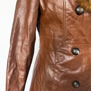 May include: A brown leather coat with a fur collar. The coat has a double-breasted design with large, dark buttons. The leather has a glossy finish, and the coat appears to be vintage.