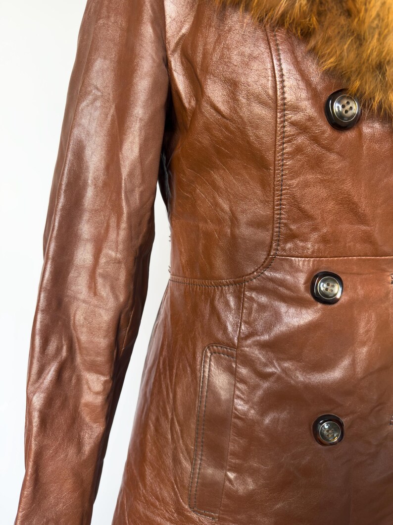 May include: A brown leather coat with a fur collar. The coat has a double-breasted design with large, dark buttons. The leather has a glossy finish, and the coat appears to be vintage.