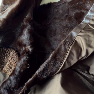 May include: Close-up of a dark brown fur coat with a satin lining. The coat features a button closure and a textured, brown collar. The fur appears soft and luxurious, suggesting a high-end garment.