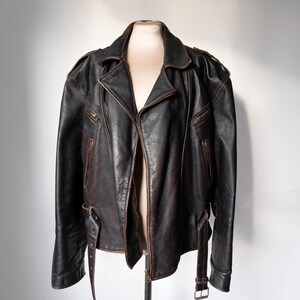 May include: A black leather jacket with a brown distressed finish. The jacket features a notched collar, asymmetrical zipper closure, and multiple zippered pockets. It has a belt at the waist and is displayed on a mannequin.