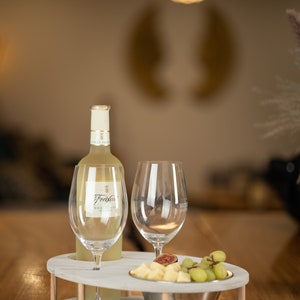 May include: A white wine bottle with a white label that says "Freixenet" on a white serving tray with two wine glasses and a bowl of fruit. The tray has a wooden base.